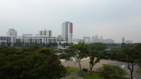 Aerial-dolly-above-tree-line-at-park-rises-to-reveal-ho-chi-minh-city-skyline-on-foggy-day