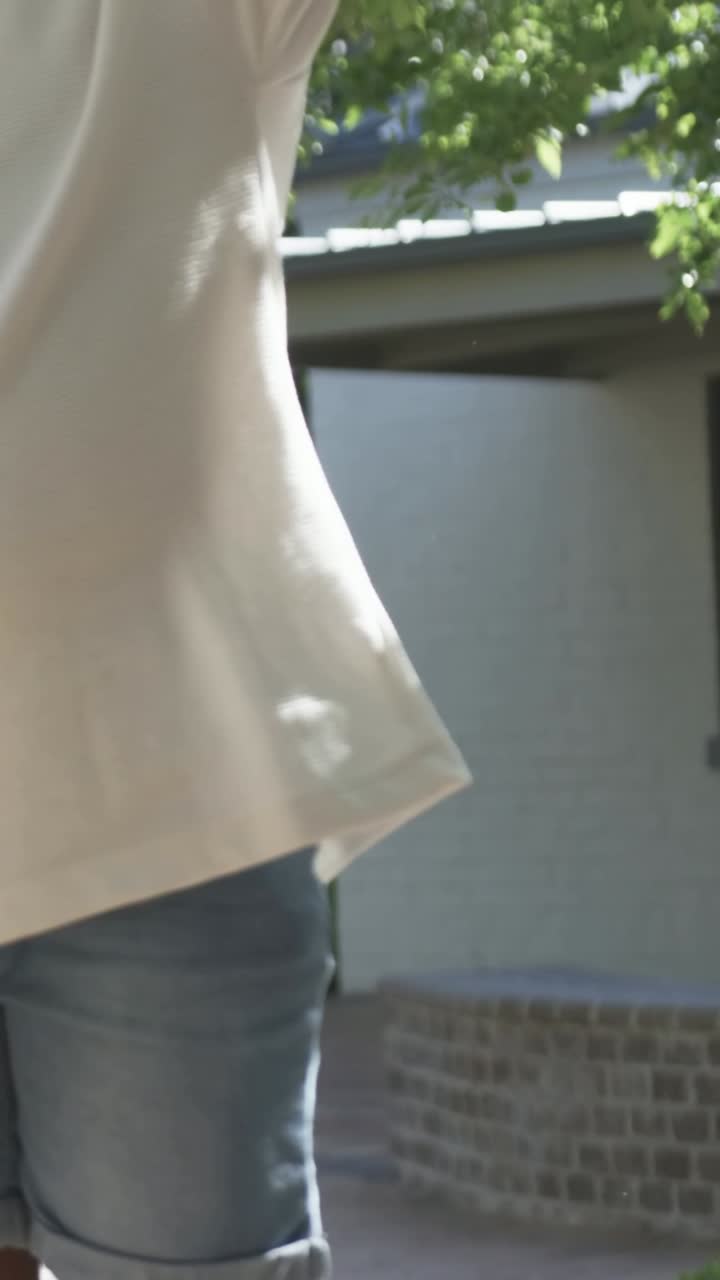Vertikales Video: Schwingender gelber Reifen kommt ins Bild, Kind führt ihn auf Gehweg, spielt im Schatten.