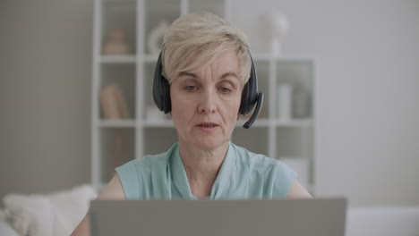 call-center woman is answering at telephone calling in tech support using laptop and headphones portrait of female worker indoors