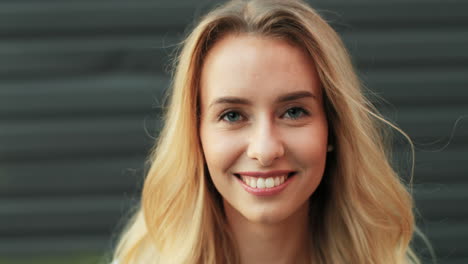 close-up view of charming young blonde woman with blue eyes looking and smiling at the camera