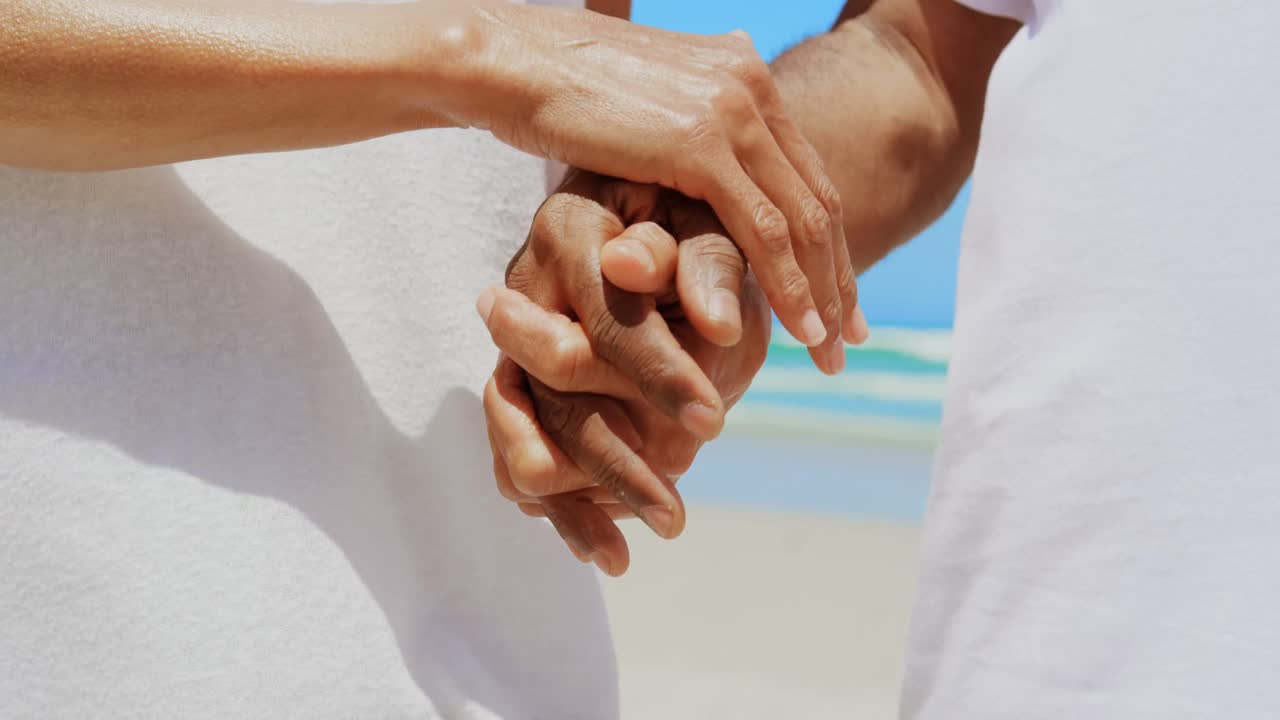 sección media de romántica activa pareja afroamericana de alto nivel cogida de la mano en la playa 4k