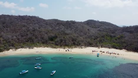 Fascinante-Toma-Aérea-Con-Drones-De-Una-Bahía-Arenosa-Con-Agua-Turquesa,-Con-Pequeñas-Embarcaciones