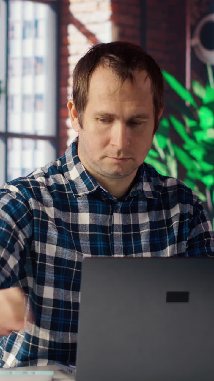 Vertical video Employee at workstation completing spreadsheets on laptop and listening music