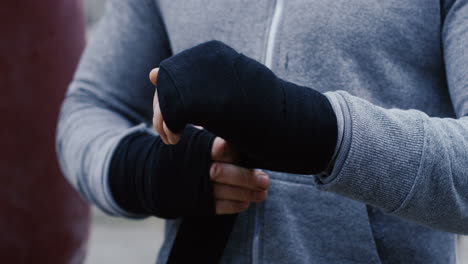 close-up view of young male boxer wrapping his hands with black cloth outdoors an abandoned factory on a cloudy morning