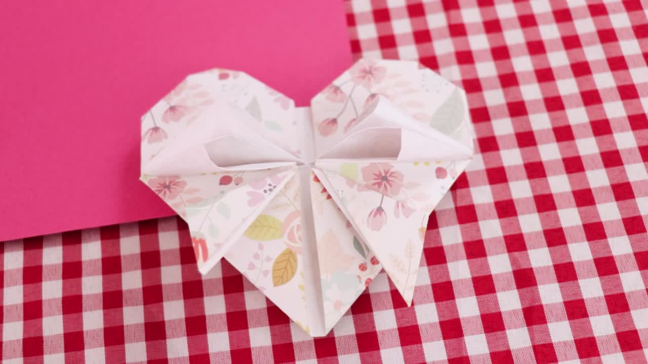 Foldet hjerte af dekorativt origamipapir på ternet dug.