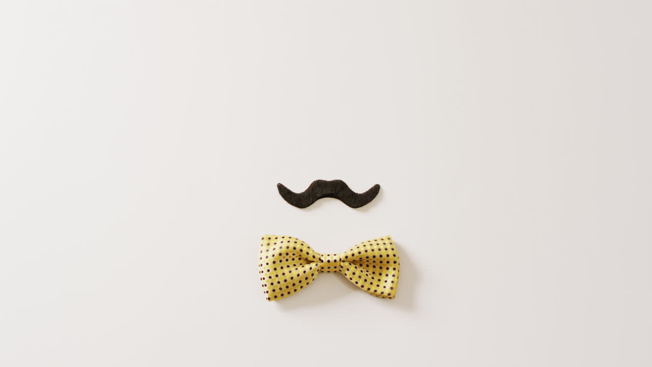 Video of black false moustache and yellow spotted bow tie on white background with copy space