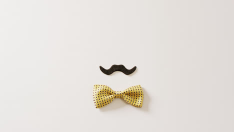 Video-of-black-false-moustache-and-yellow-spotted-bow-tie-on-white-background-with-copy-space