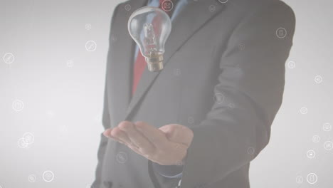 animation of media icons floating over midsection of businessman throwing and catching lightbulb