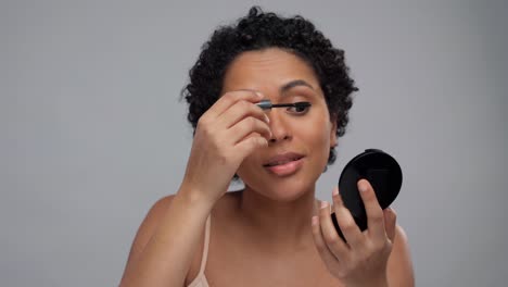 Schönheit,-Make-up-Und-Kosmetik-Konzept-Lächelnd-Schöne-Junge-Afroamerikanische-Frau-Anwendung-Mascara-über-Grauem-Hintergrund