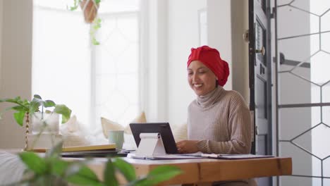 Video-De-Una-Mujer-Birracial-Feliz-Con-Hijab-Sentada-En-El-Escritorio-Haciendo-Videollamadas-Con-Tableta-En-Casa,-Espacio-Para-Copiar