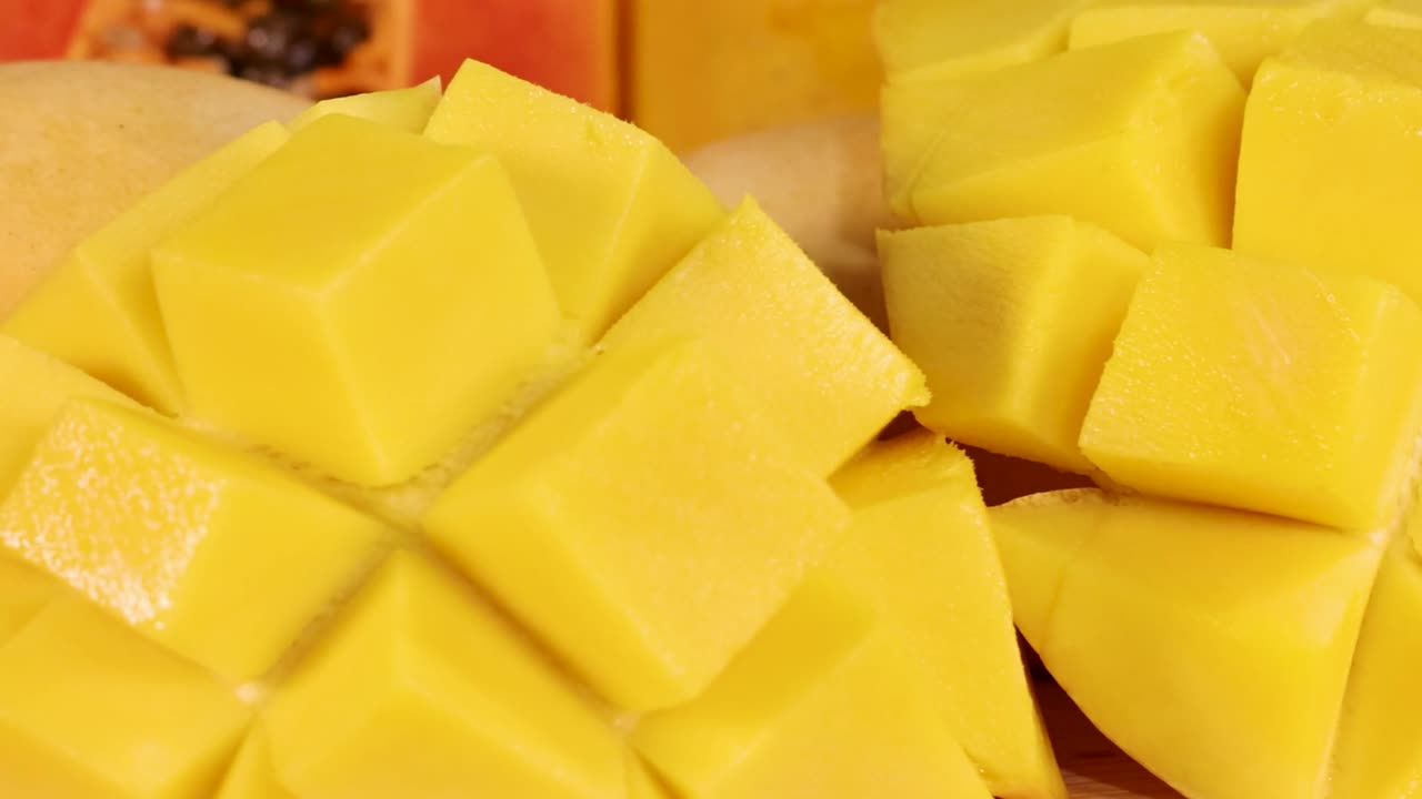 En detaljert nærbilde-tagning som panorerer over skivet mango, kiwi, sitroner, jordbær og røde epler