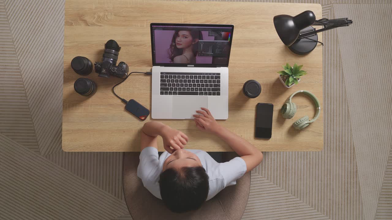 Top View Of Asian Woman Editor Thinking About The Idea Then Raising Index Finger While Sitting In The Workspace Using A Laptop Next To The Camera Editing Photo Of A Woman At Home