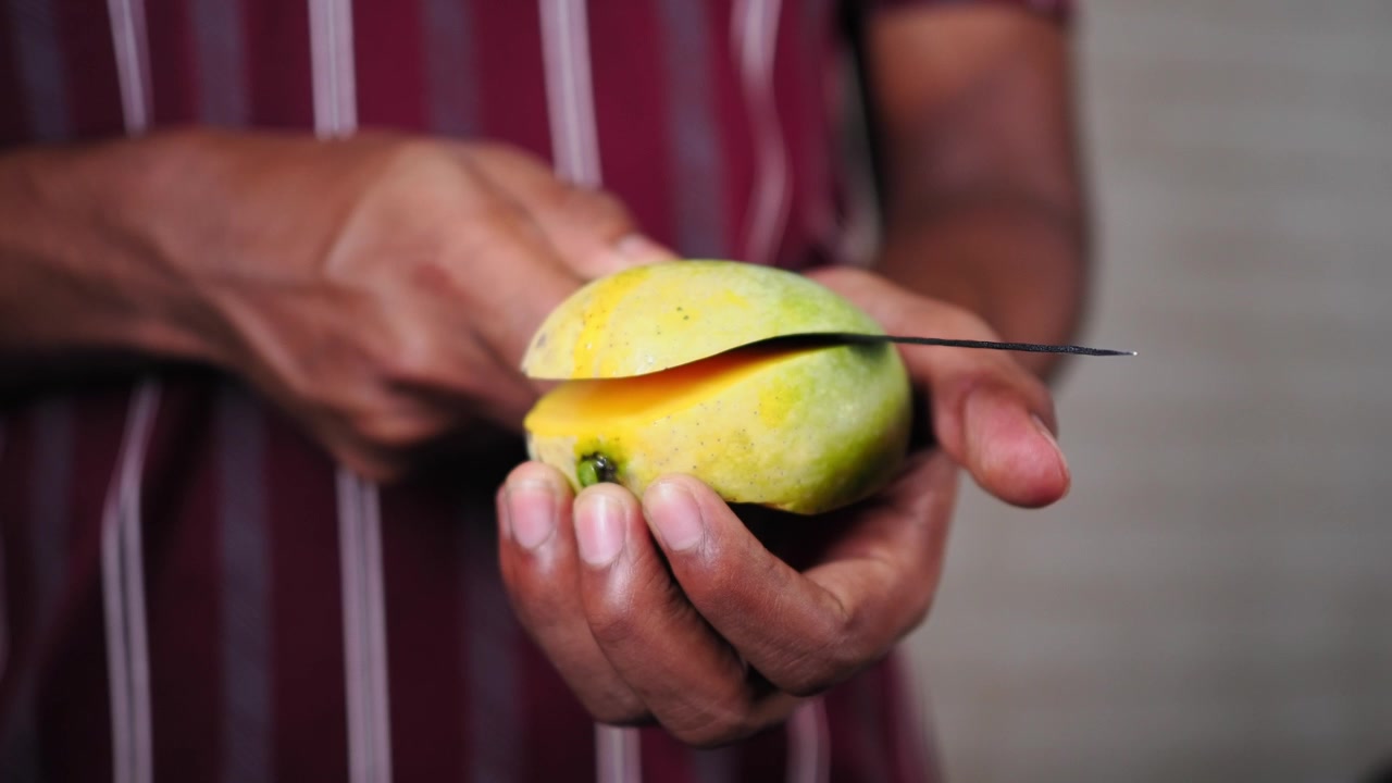 Persona che affetta un mango fresco con un coltello.