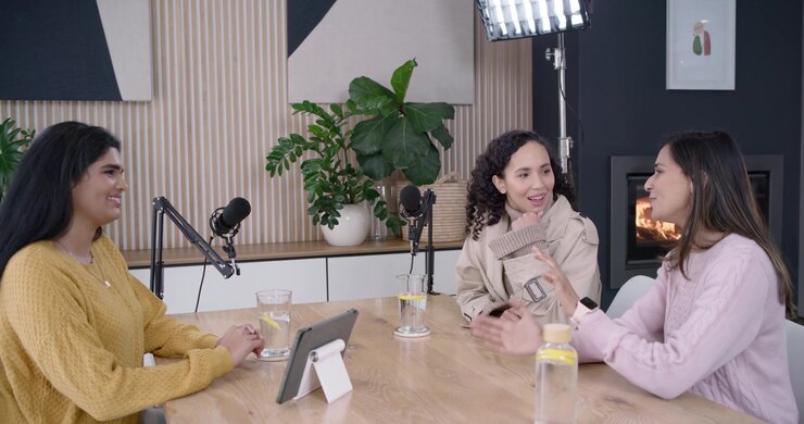Diverse female hosts in mustard knit beige trench hosting podcast after mic check using mics