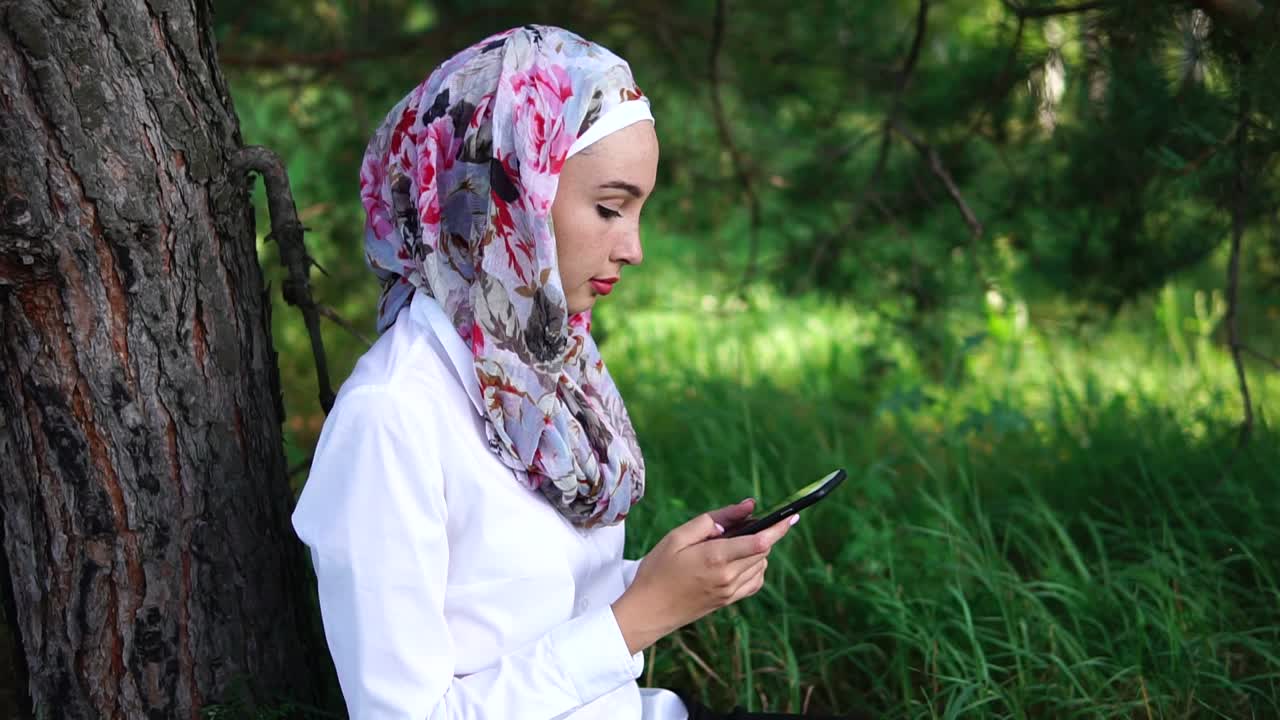 Woman with hijab using phone in a forest