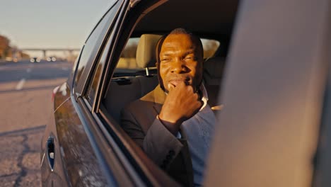 a confident man with black skin opens the rear window in a modern car and looks out of it during his trip and business trip outside the city
