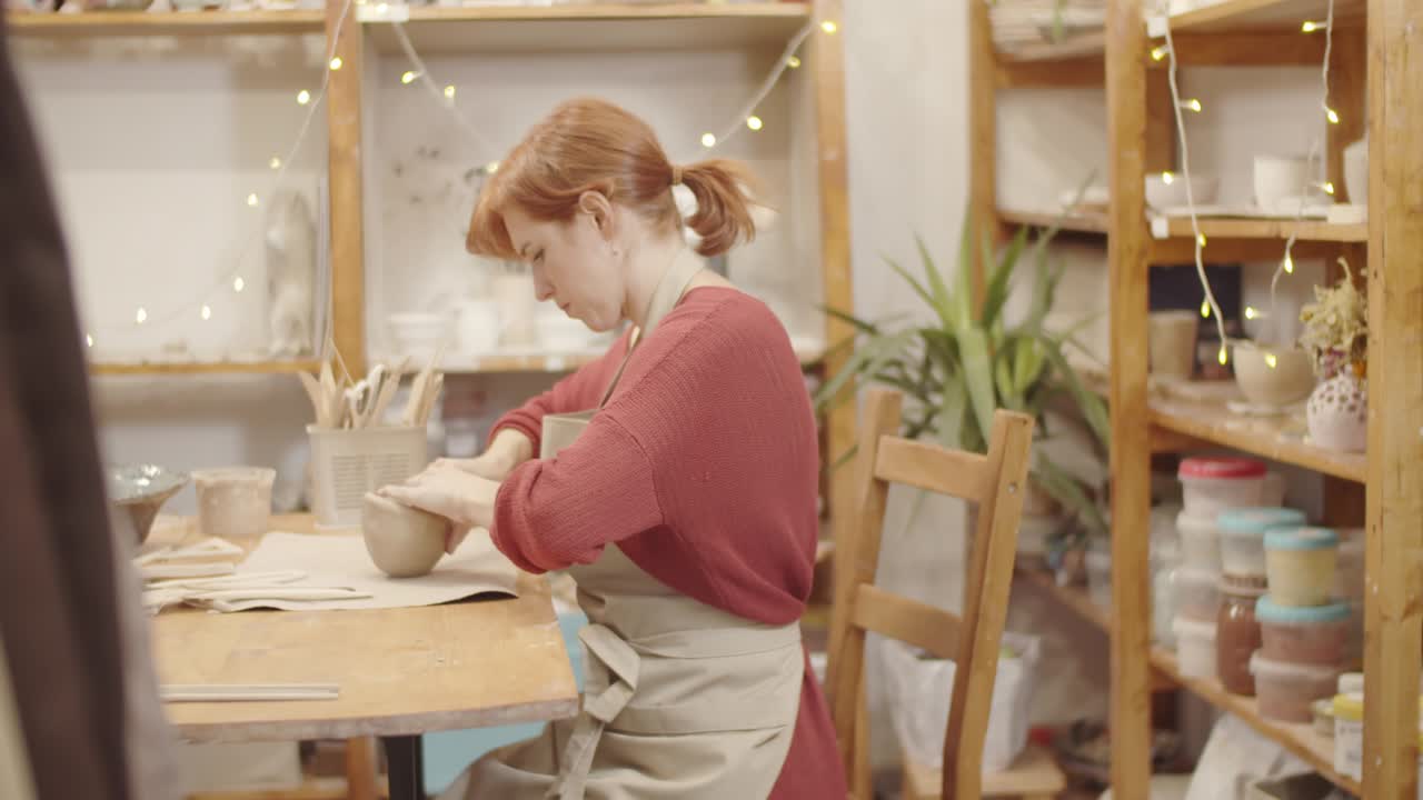 Jonge Kaukasische vrouw die een kleikom vormt in een pottenbakkersatelier.