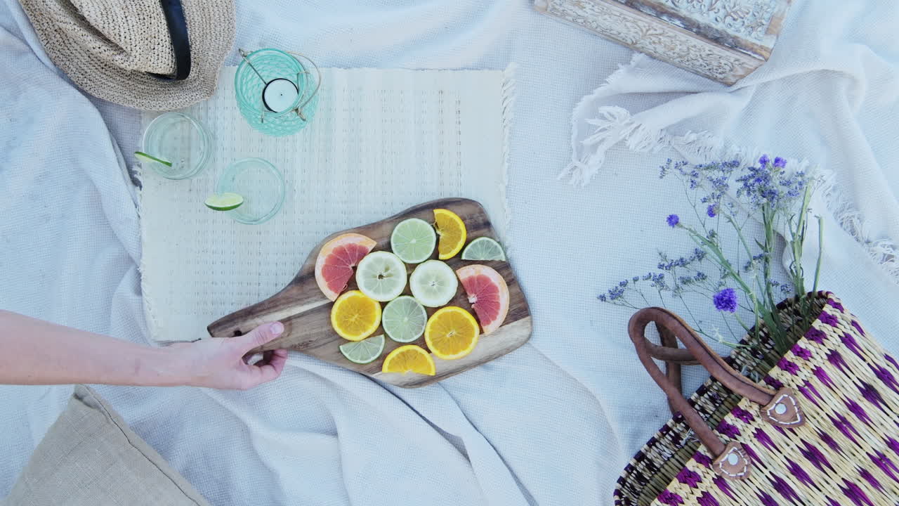 Hand Taking A Wooden Picnic Board on picnic rug With Beautiful citrus Fruit Slices - Close Up Shot