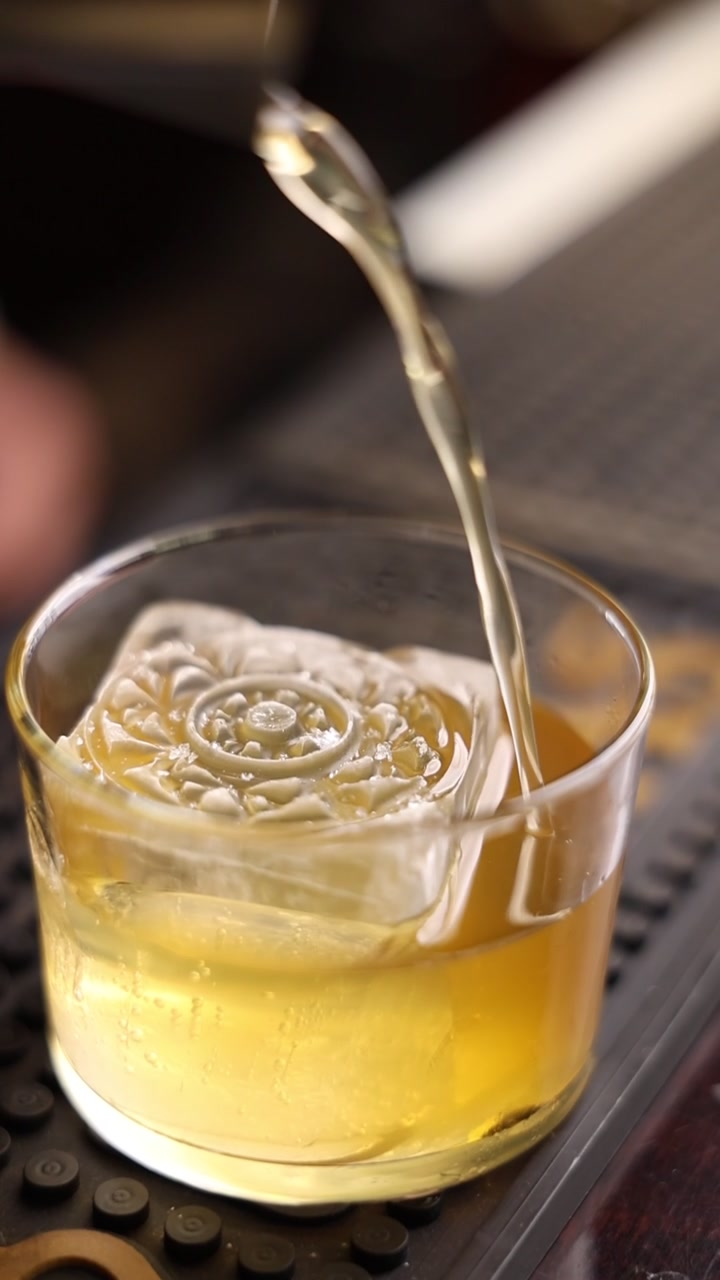 Barman che versa un cocktail dorato su un cubetto di ghiaccio decorativo