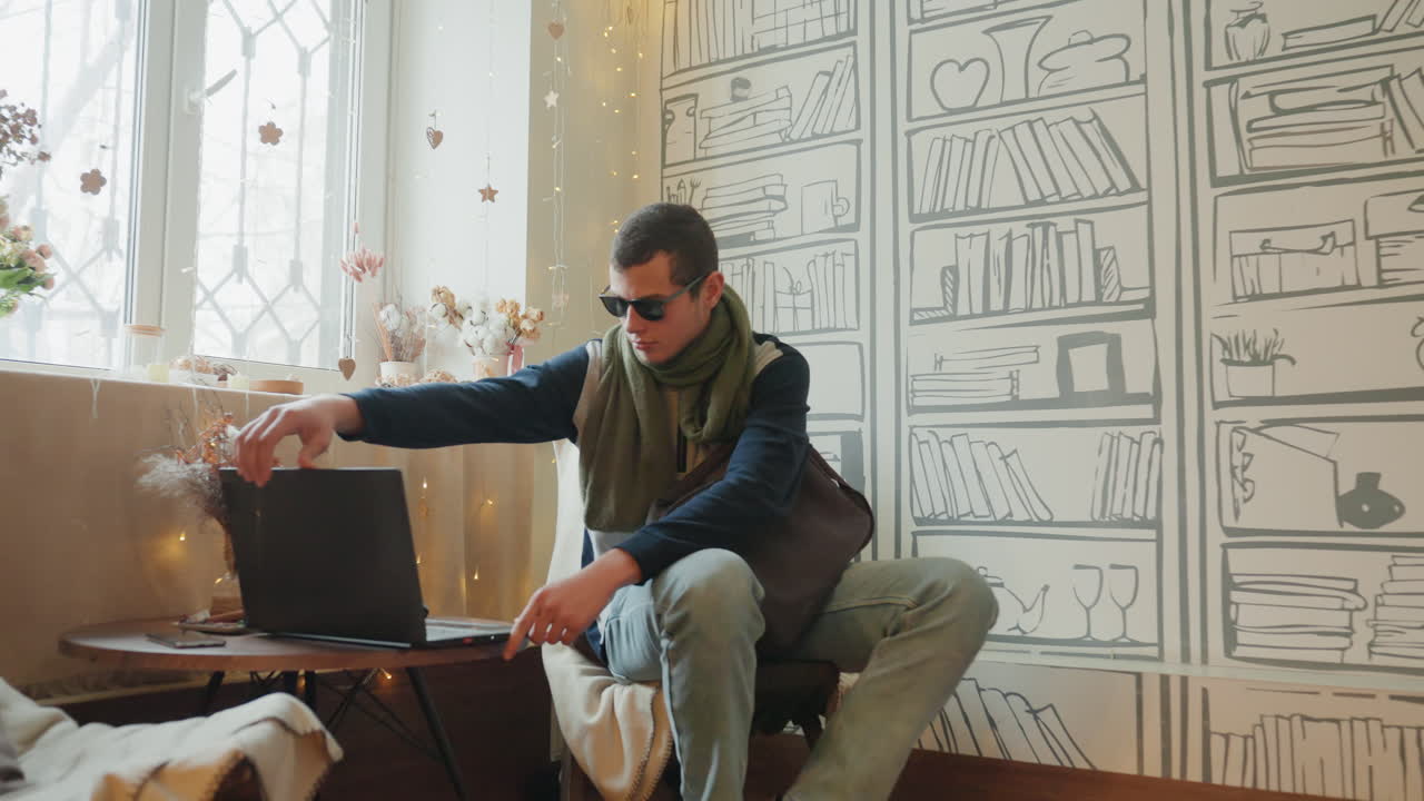 White man working laptop in livingroom. Sipping coffee, making quick phone call, adjusting bag on sofa, connecting charger to laptop, hands typing on keyboard, focused expression, modern boho