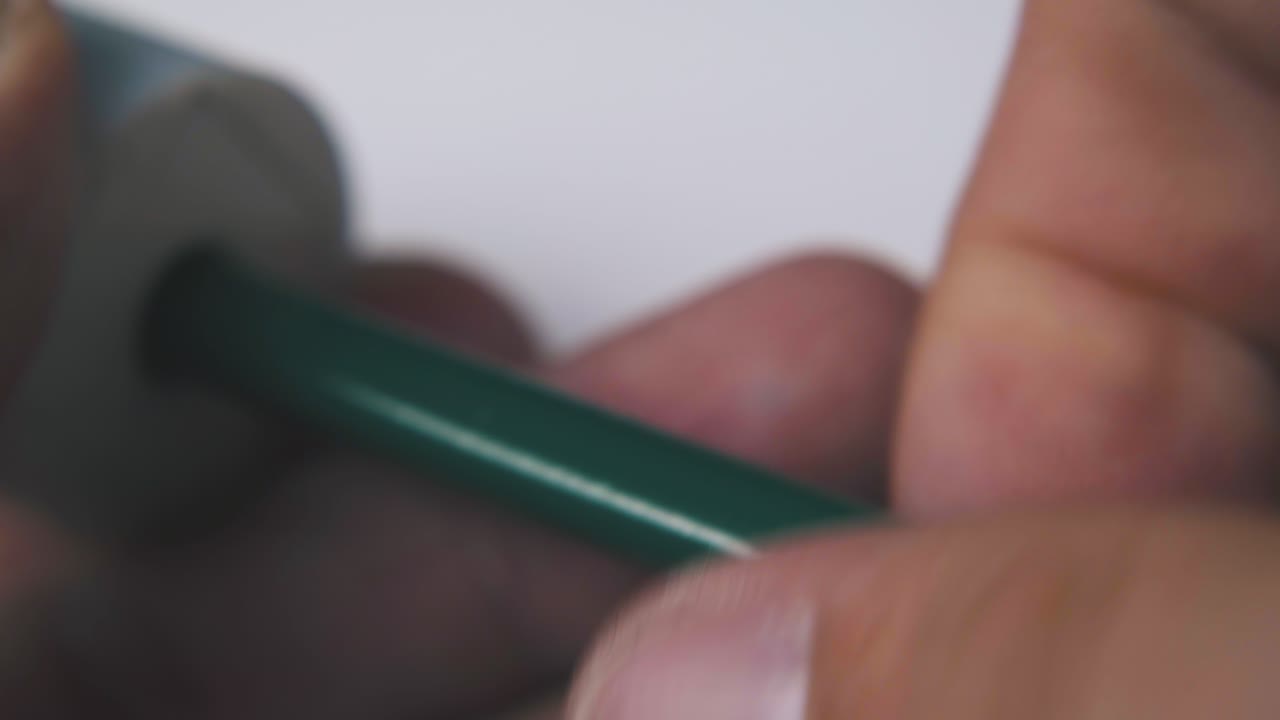 el hombre gira el lápiz verde sosteniendo el afilador en un fondo claro