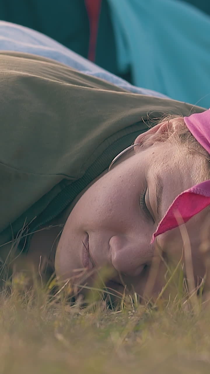 young plump woman with hangover drinks water from metal cup lying on brown meadow slow motion closeup