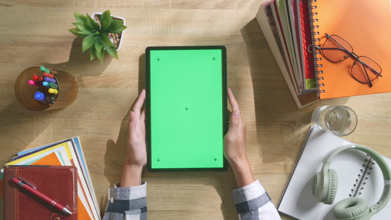 vista de arriba hacia abajo de una computadora portátil con pantalla verde simulada pantalla chromakey en un escritorio de oficina de madera al lado de la libreta con bolígrafos, gafas y un vaso de agua.