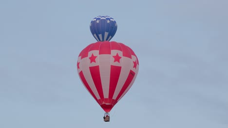 a dynamic scene as one hot air balloon slowly moves, revealing another balloon behind it in the clear sky at the canberra balloon spectacular.