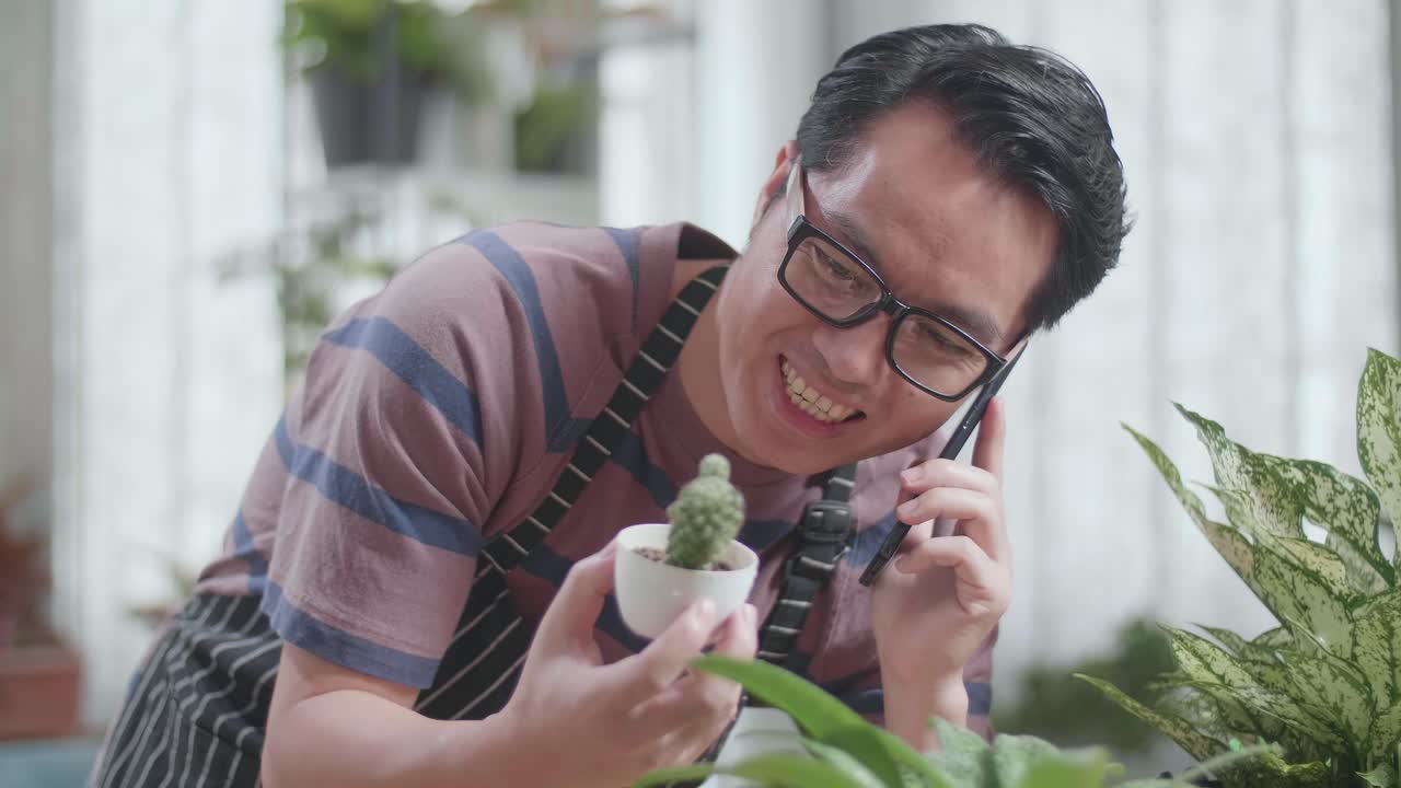 un hombre asiático con plantas hablando por teléfono en casa.