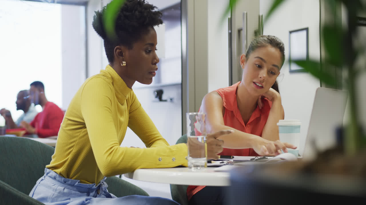 Diverse female business colleagues talking and using laptop in office