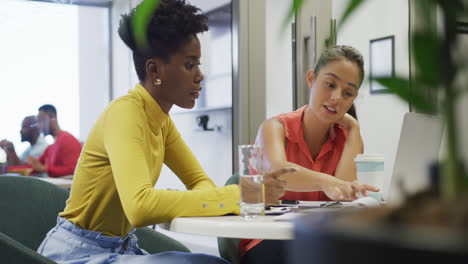 diverse female business colleagues talking and using laptop in office
