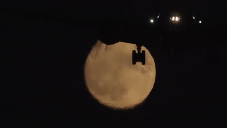 airplane silhouetted against a full moon at night
