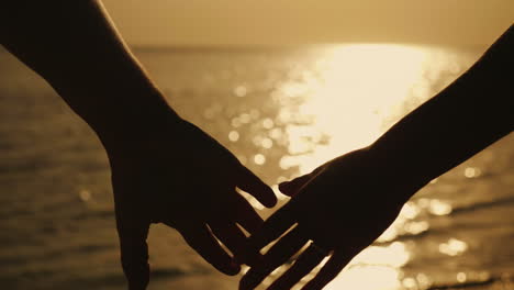 hands of a man and a woman against the background of the sea and the setting sun 4k slow motionvideo