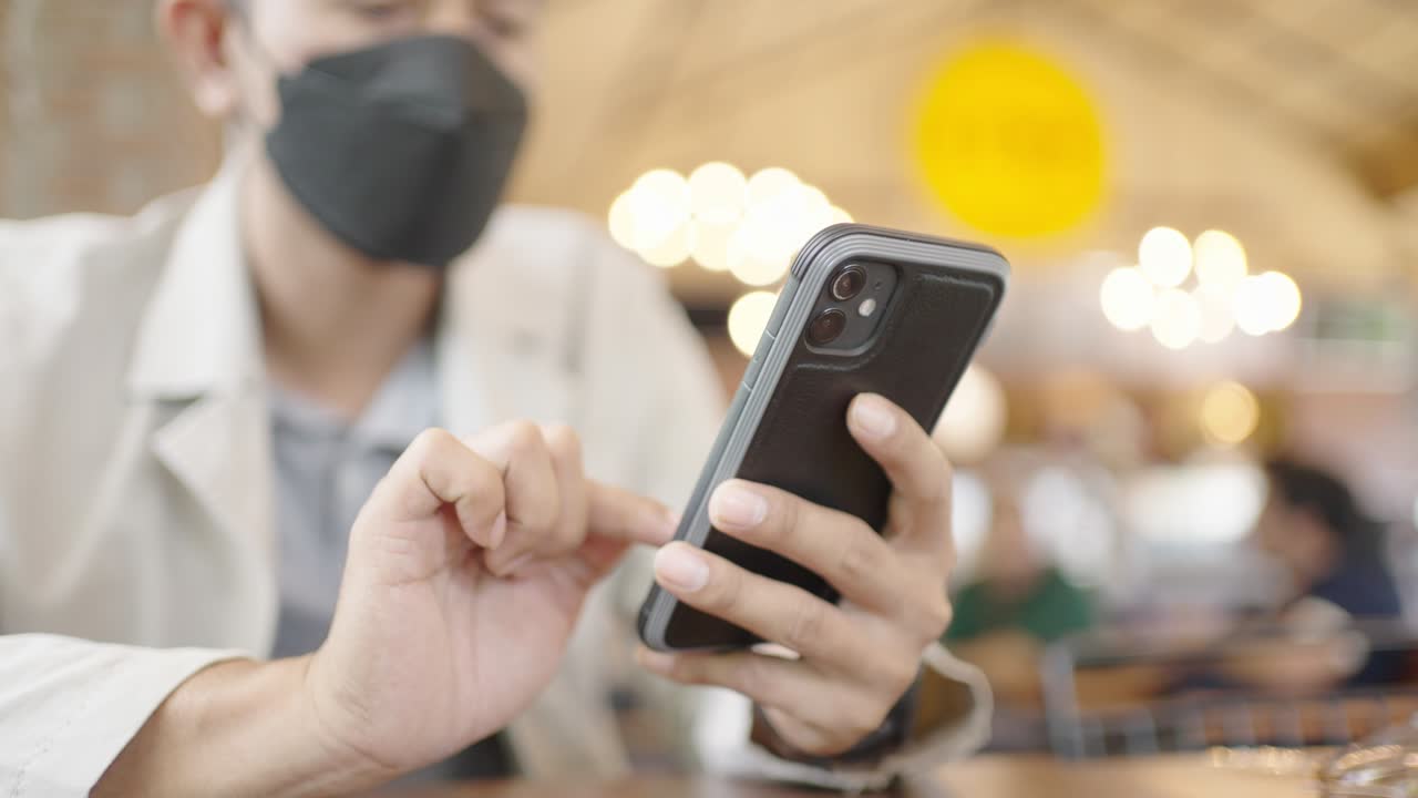 수술 마스크를 착용한 젊은 사업가가 인터넷에 연결된 스마트 폰을 통해 고객들과 비디오 컨퍼런스를 하고 있습니다.