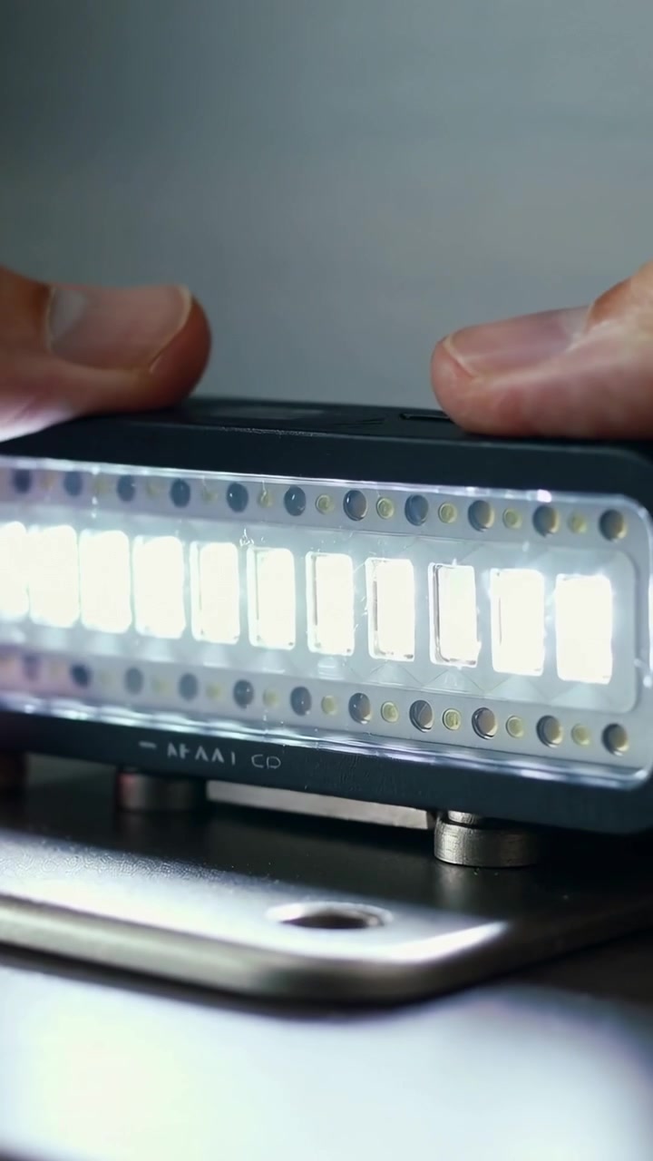 Vertical video: Entering adult hands placing LED module onto metal base at bench, securing magnets