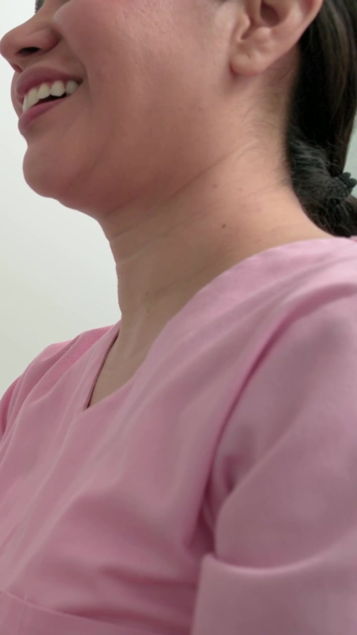 Video verticale: Donna adulta che si gira e risponde a una voce fuori campo in una stanza, con camice rosa e elastico per capelli