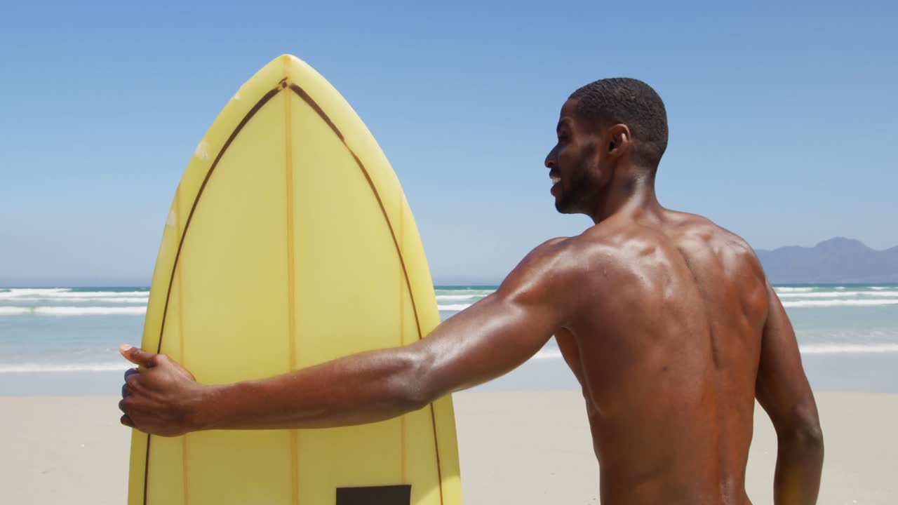 Mies surffaaja seisomassa surffilaudan kanssa rannalla 4k