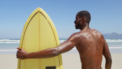 surfista masculino de pie con una tabla de surf en la playa 4k
