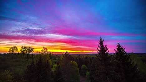 the sky above a forest changes from yellow and orange colors to blue and purple in a beautiful time lapse