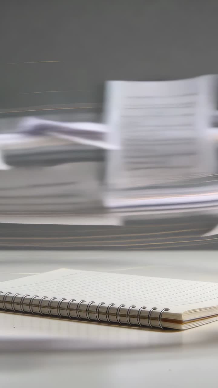 Vertical video: Sudden gust sending loose white sheets moving across desk, passing spiral notebook