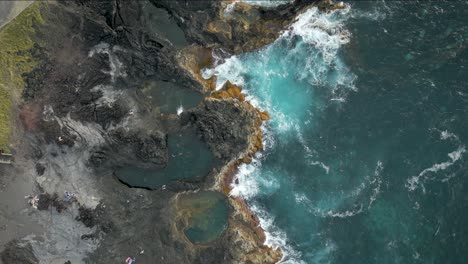 Top-down-aerial---people-swim-in-natural-pools-of-Mosteiros,-São-Miguel,-Azores