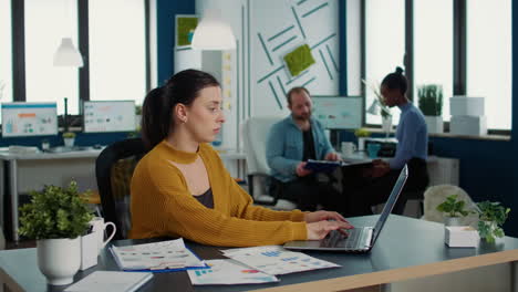 Focused-startup-employee-typing-using-laptop-keyboard-while-looking-at-screen-and-smiling-sitting-at-desk