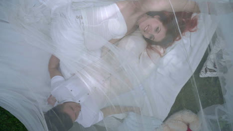 top view of love couple relaxing on white fabric behind transparent veil in park