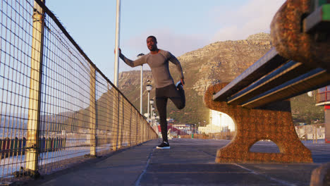 Focused-african-american-man-stretching,-exercising-outdoors-by-seaside