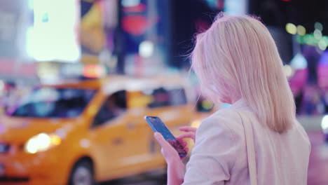 business woman uses a smartphone on busy times square in new york the famous yellow cabs are passing