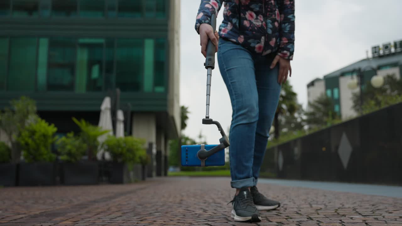 Kvinne bruker teleskopisk uttrekkbar gimbal-stabilisator med mobiltelefon montert for å filme på gulvnivå