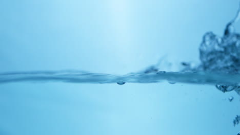 Close-up-shot-of-crystal-clear-blue-waters-bursting-into-waves,-creating-splatters-and-bubbles-in-a-big-water-tank