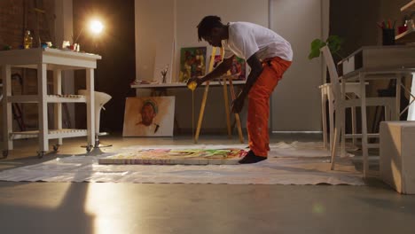 artista masculino afroamericano vertiendo pintura en lienzo y pintando en un estudio de arte