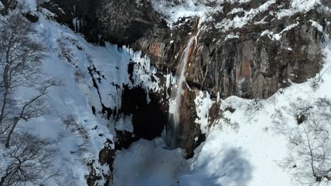 Toma-Estática-De-Una-Cascada-De-Nieve-Derretida,-Cámara-Volando-A-Través-Del-Desfiladero-Revelando-El-área-De-La-Cascada