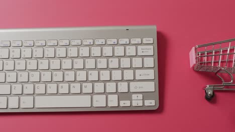 Overhead-view-of-computer-keyboard,-shopping-trolley-on-pink-background